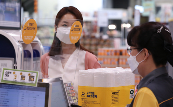 A cashier checks out goods behind a protective plastic shield to minimize the risk of coronavirus infection on Monday at Emart's Seongsu branch in eastern Seoul. Emart announced it would to install plastic shields in 155 different branches nationwide after introducing them in Daegu and North Gyeongsang branches last month. [YONHAP]