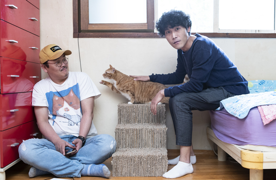 Producer Cho Eun-sung,left, and director Lee Hee-seop of the cat documentary "Our Cats" pose for a photo in Lee's home along with his cat and roommate, Lenny. [KWON HYUK-JAE] 