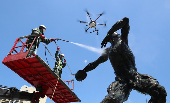 Officials from the Songpa District Office use drones and high-pressure power washers to clean an Olympic sculpture in Olympic Park in Songpa District, southern Seoul, on Monday. The district office cleaned 50 Olympic sculptures installed between Jamsil Sports Complex and Olympic Park on Monday. [YONHAP]