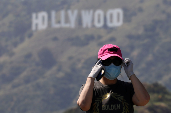 A person wearing a face mask and gloves stands in front of the Hollywood sign after a partial reopening of Los Angeles hiking trails during the outbreak of the coronavirus disease at Griffith Park in Los Angeles, May 9, 2020. [REUTERS/YONHAP]