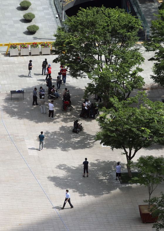 People stand under shade of trees to avoid direct sunlight at Seoul Plaza in front of Seoul City Hall on Monday during the heat of the day. [YONHAP]