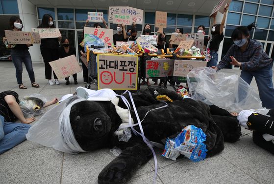 Activists hold a performance calling for an immediate ban on the repackaging of packaged products after a press conference in front of Emart’s Seongsu branch in eastern Seoul on Thursday. Organized by nonprofit organizations including Green Korea and Green Future, the conference follows a government decision in late June to postpone a ban on retailers selling promotional repackaged bundles. [YONHAP]
