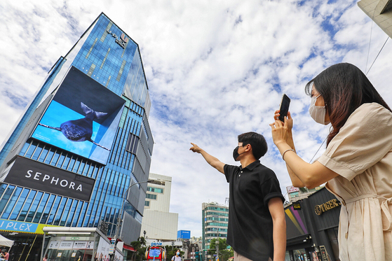 Passersby take photos of a media art piece showcased via a digital sign on an outer wall of the Hyundai U-Plex Department Store in Sinchon, western Seoul, on Wednesday morning. [YONHAP]