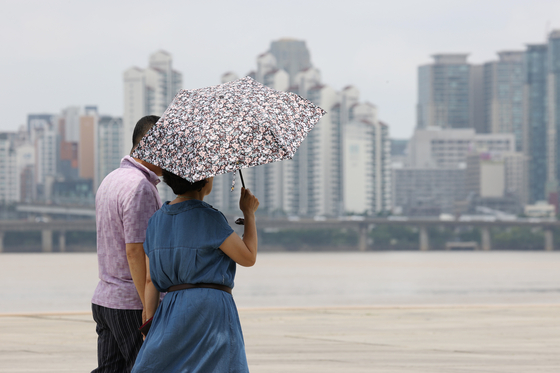 A woman carries a sun parasol in Yeouido Hangang Park, western Seoul, on Sunday, as the record-long monsoon season ends and a heat wave begins. [YONHAP]