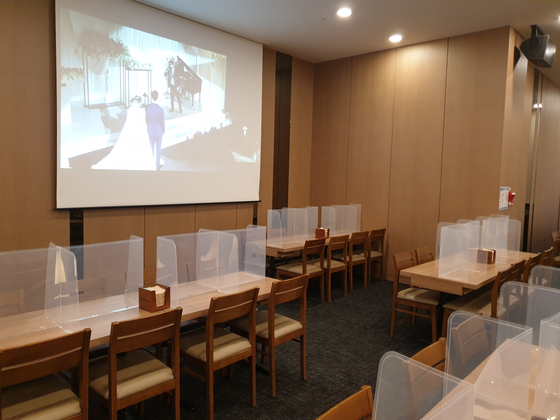 A real-time display of the wedding plays on a large screen on Sunday at the banquet hall of a wedding venue in Seoul. Since the initiation of Level 2 social distancing, all buffet services have stopped. [JEONG JIN-HO]