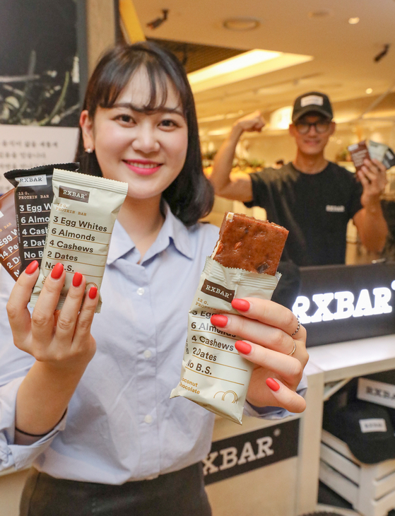 A model holds up RXBAR protein bars at Hyundai Department Store's Coex branch in southern Seoul on Tuesday. Seattle-based RXBAR makes protein bars excluding artificial sweeteners including sugar. [HYUNDAI DEPARTMENT STORE]