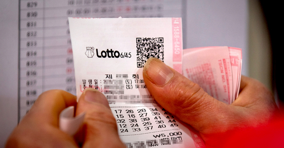 A person is checking their Lotto lottery ticket with the winning numbers. [YONHAP] 