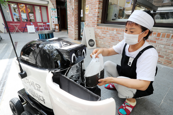 A restaurant employee in Suwon, Gyeonggi, puts food into a delivery robot in August. [NEWS1]