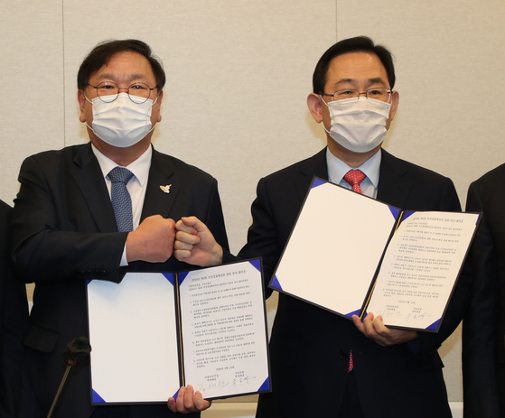 From left, Democratic Party floor leader Kim Tae-nyeon and People Power Party floor leader Joo Ho-young, fist bump while holding an agreement on the fourth supplementary budget at the National Assembly in Seoul on Tuesday. [YONHAP]