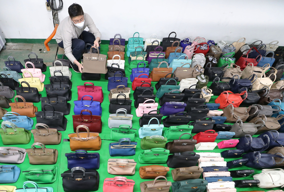 An employee shows confiscated knockoff luxury handbags at the Seoul Main Customs building in Gangnam District, southern Seoul. Seoul Main Customs announced on Wednesday that it caught a pair of siblings illegally distributing 29 billion won ($25 million) of fake merchandise and sent the case to the prosecution. [YONHAP]