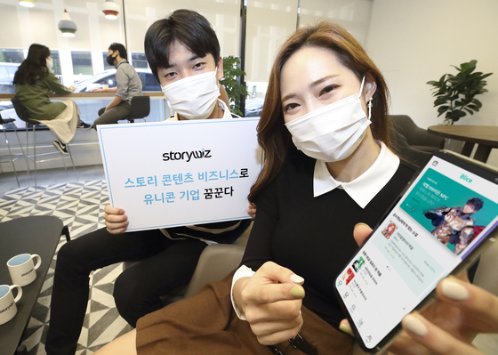 Models hold up a mobile phone with the app for Blice on Tuesday, prior to the press conference held at Gwanghwamun, central Seoul. Blice is a web novel platform run by Storywiz. [KT]