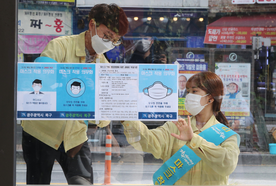 Gwangju officials tape fliers to a bus stop near Chonnam National University Tuesday informing the public about a new law on face masks. [YONHAP]