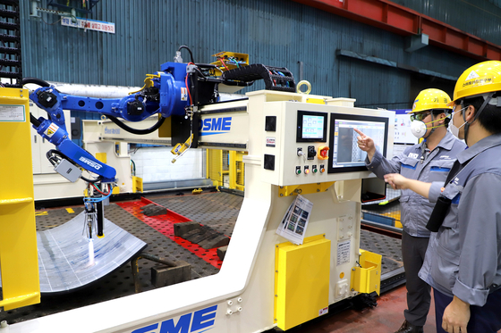 Daewoo Shipbuilding & Marine Engineering workers stand in front of the company’s artificial intelligence (AI)-maneuvered hot working robot. The shipbuilder on Tuesday said it has developed the world’s first AI-operated metalworking robot for constructing ships. The robot, called Goknuri, is installed at the shipyard in Geoje Island, South Gyeongsang. [YONHAP]