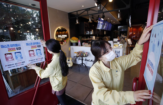 Gwangju health officials post fliers in a coffee shop Thursday informing the public they could face penalties for not wearing masks in public. [YONHAP]