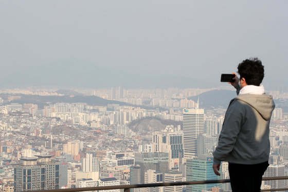 A man takes a photo of downtown Seoul from a trail on Mount Namsan on Tuesday as fine dust partially obscures the view. [JANG JIN-YOUNG]
