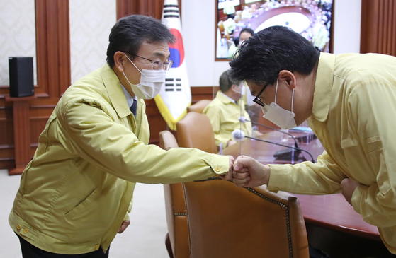 Newly appointed Health and Welfare Minister Kwon Deok-cheol, left, bumps fists during a government meeting on Covid-19 measures on Thursday.  [YONHAP] 