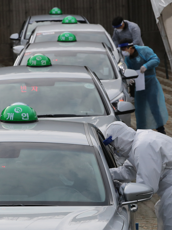 Medical workers extract samples from taxi drivers at a drive-thru testing site in Asiad Main Stadium in Busan on Monday, in a pre-emptive measure to detect Covid-19 infections among taxi drivers. [SONG BONG-GEUN]
