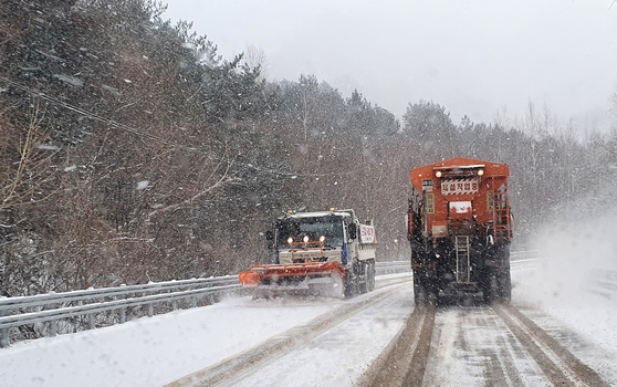 Snow plough trucks clear snow piled on the road in Yangyang County, Gangwon, on Monday after a heavy snowfall warning was issued in the area. [YONHAP]