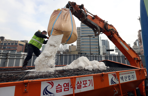 Workers unload calcium chloride on snowplow trucks in Jongno District, central Seoul, Wednesday to prepare for heavy snowfall as forecast by the weather agency. [YONHAP]