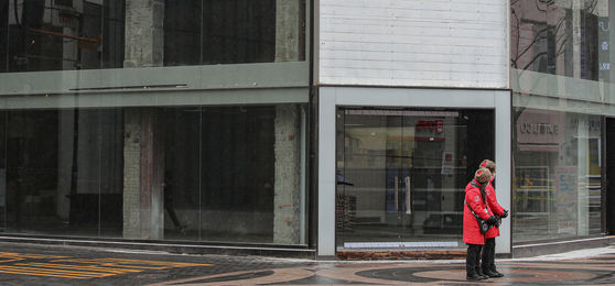 Seoul city government tour guides await tourists in front of an empty store in Meyong-dong on Feb. 16. Because of Covid-19, stores have shut down and people lost their jobs, increasing dependence on government support. [YONHAP]