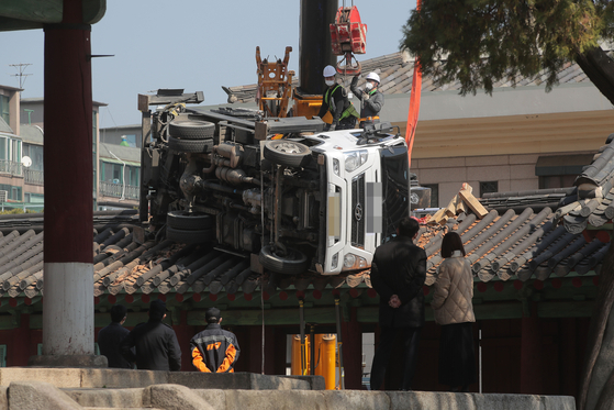 Workers prepare to lift a ladder truck that fell on the roof of the Dongsam Gate of the Confucian Shrine in Sungkyunkwan University in Jongno District, central Seoul, on Monday. The gate is Korea's Treasure No. 141. A crane truck dropped the ladder truck, which was supposed to prune branches of Natural Monument No. 59, a gingko tree at the shrine. [YONHAP]