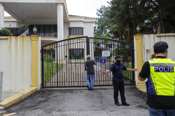 A man locks the gates of the North Korean embassy in Kuala Lumpur, Malaysia, as police guard the premises Sunday. Pyongyang’s diplomats and their families departed Kuala Lumpur Sunday after North Korea and Malaysia severed diplomatic ties over the extradition of a North Korean businessman, Mun Chol-myong, to the United States over money laundering charges. [EPA/YONHAP]