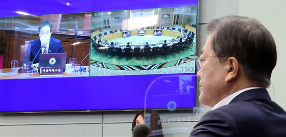 President Moon Jae-in, right, exchanges greetings with Seoul Mayor Oh Se-hoon, shown left in the screen hung on the wall, during the video conference cabinet meeting on Tuesday. Moon joined the meeting from the Blue House, while Oh and some other ministers joined from the government complex buildings in Seoul and Sejong. [YONHAP]