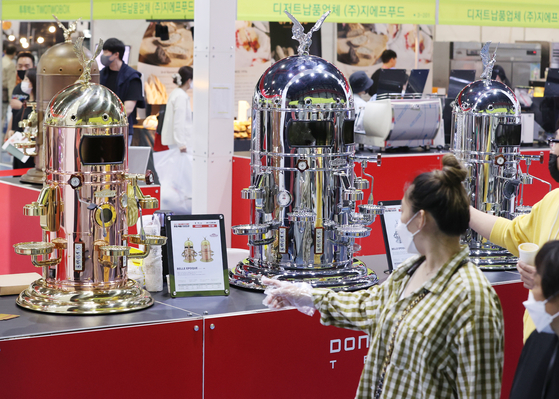 A customer checks out a coffee machine at the Seoul Cafe and Bakery Fair held at Setec in Seoul on Thursday. [YONHAP]