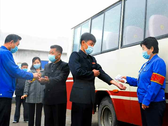 North Koreans in masks get temperature checks before boarding a bus in Pakchon County in North Pyongan, pictured in an article run by the state-run Rodong Sinmun on Covid-19 quarantine measures Tuesday. Pyongyang claims that it has no Covid-19 cases. [RODONG SINMUN]