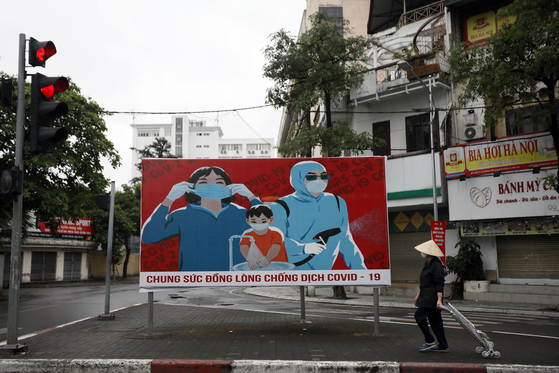 A woman walks past a sign about the Covid-19 pandemic in Hanoi, Vietnam, on April 23, 2020. Communist propaganda, which was most visible during the Vietnam War, has been revived in recent weeks as artists contribute to the national effort to fight the coronavirus. [EPA/LUONG THAI LINH/YONHAP]