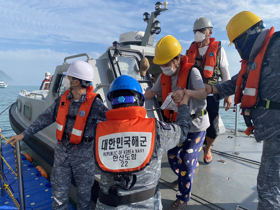 Helped by sailors, a resident from a remote island arrives on Korea's first military training vessel, Hansando, off Jin Island, South Jeolla, on Tuesday. The Navy has conducted an operation to help residents from remote islands, devoid of medical facilities, receive Covid-19 vaccine shots at a mass vaccination center installed on the ship. [YONHAP]