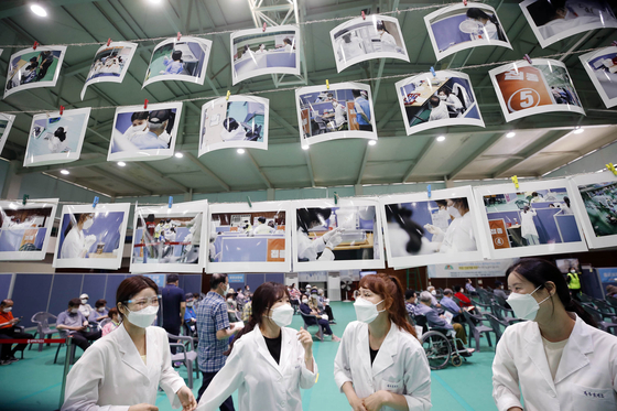 Health workers look at photos hung inside the vaccination center in Gwangju on Monday, after the district office installed a photo exhibition to thank the medical staff for their hard work during the Covid-19 pandemic. [NEWS1]