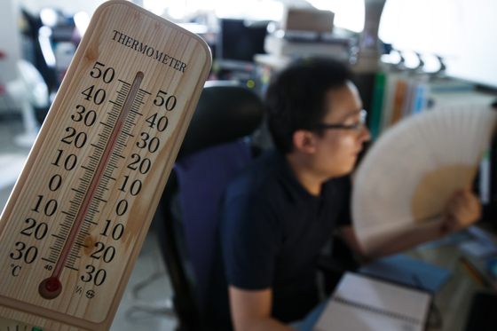 In this file photo, a government worker uses a fan as the air conditioning system of the government complex in central Seoul is shut down to prevent a blackout on Aug. 13, 2013. The room temperature was 34 degree Celsius without air conditioning.  [NEWS1] 