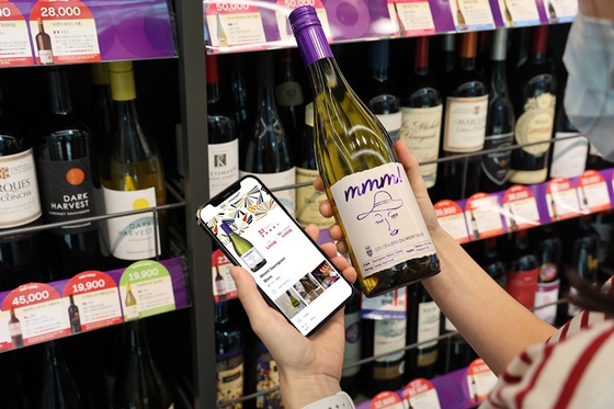 A customer holds a wine bottle to look for information on the soon-to-launch wine curation service on convenience store CU's mobile app Pocket CU. [BGF RETAIL]
