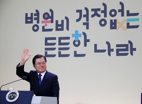 President Moon Jae-in waves his hand at participants in the virtual event to commemorate the fourth year since the introduction of Mooncare, a policy of lowering medical costs for the general public, at the Blue House on Thursday. [JOINT PRESS CORPS]