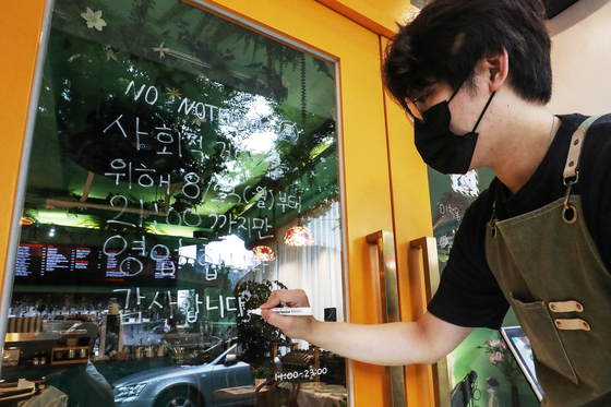 An employee at a coffee shop in Seoul writes a notice on Sunday explaining new social distancing rules to take effect the following day, which would limit business hours of restaurants and cafes in areas under Level 4 to 9 p.m. from the current 10 p.m. [NEWS1]