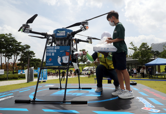 A boy receives a pizza delivered by a drone at Sejong Lake Park in Sejong City on Sunday. It was the first demonstration of a commercial drone delivery in collaboration with the drone start-up P-square and Domino’s Pizza. The Transportation Ministry said it could expand the zone for drone delivery after evaluating the pilot project through the end of October.  [NEWS1]