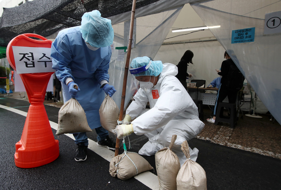 Medical workers deploy sand bags at tents for Covid-19 testing in Gwangju on Monday as winds picked up as Typhoon Omais approached the Korean Peninsula. [YONHAP]