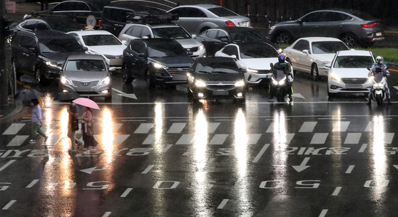 Passenger cars, with their headlights turned on, wait at a traffic light near Seoul City Hall on Tuesday as it gets dark early, owing to rain clouds. [YONHAP]