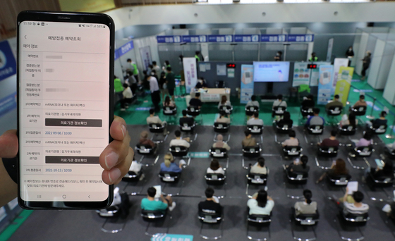 Patients wait for any adverse reactions after their vaccinations at a local gym in Seodaemun District, western Seoul, on Tuesday afternoon. The screen of the mobile phone being held up shows the vaccination registration information of an unidentified person. [NEWS1]