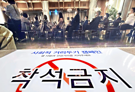 Eased restrictions for weddings were part of the changes for social distancing guidelines announced by the government for the next two weeks through Oct. 17. The photo shows a wedding in Seoul on Sunday and a sign that reads, "Do not sit here" to enforce social distancing. [YONHAP]