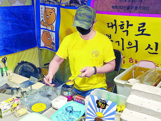 An Sae-hwan, 37, is making dalgona (a thinly spread Korean sugar candy with a stamped outline of a random shape) inside his 2-square-meter (22-square-foot) candy stand near Hyehwa Station in eastern Seoul on Monday evening. His candy stand distributed the candies to the production team of the viral Netflix Korea original series, “Squid Game.” [JOONGANG ILBO]
