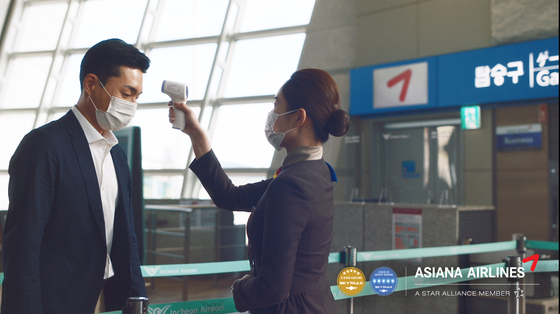 An Asiana Airlines flight attendant takes the temperature of a passenger. [ASIANA AIRLINES]
