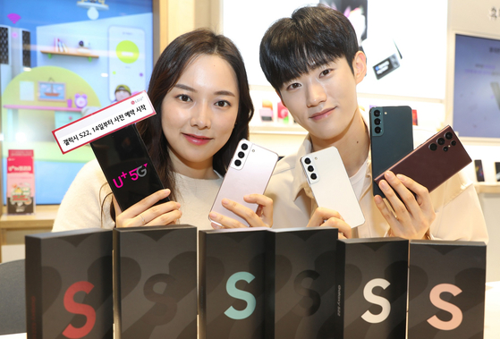 Staffers at LG U+ hold up the new Galaxy S22 smartphones. Telecom companies are offering a bundle of benefits to people who place their orders from Feb. 14 to 21. [LG U+]