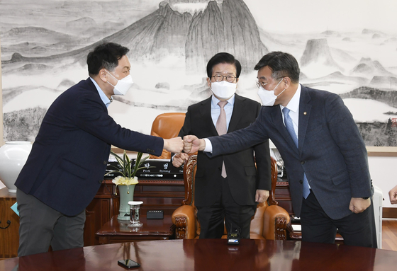 Yun Ho-jung, right, floor leader of the ruling Democratic Party, bumps fists with Kim Gi-hyeon, floor leader of the main opposition People Power Party, with National Assembly speaker Park Byeong-seug, center, watching as the two sides discussed a supplementary budget bill to provide Covid-19 relief for small businesses at the National Assembly Monday. Talks later fell apart. [JOINT PRESS CORPS]