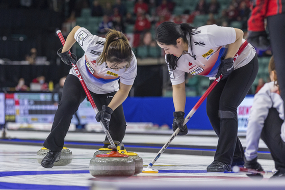 Lead Kim Seon-yeong, left, and third Kim Kyeong-ae sweep in front of a stone entering the house during a game against Canada at the World Women's Curling Championship in Prince George, British Columbia on Saturday. [AP/YONHAP]