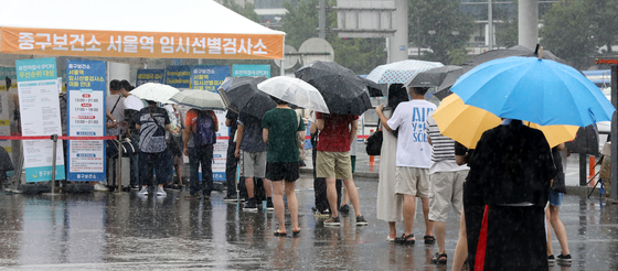 Umbrellas in hand, people line up in front of a Covid-19 testing center in front of Seoul Station in Jung District, central Seoul on Sunday afternoon. [NEWS1] 