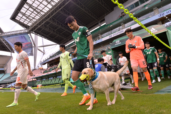 Jeonbuk Hyundai Motors players enter Jeonju World Cup Stadium on Saturday with a dog to promote dog blood donation ahead of a match against Jeju United. The muzzle the dog is wearing is the same kind worn when dogs donate blood. [NEWS1] 