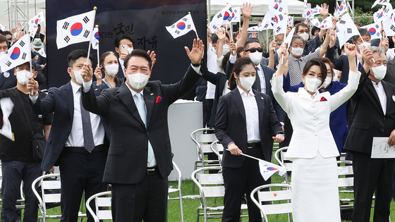 President Yoon Suk-yeol, left, and first lady Kim Keon-hee wave Korean flags during a ceremony marking the 77th Liberation Day on the front lawn of the presidential office in Yongsan District, central Seoul, on Monday. [JOINT PRESS CORPS]