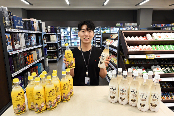 A Homeplus employee holds up an HBAF Honey Butter Almond makgeolli bottle, left, at a flagship store that opened at the retailer’s branch in Gangseo District, western Seoul, on Tuesday. The rice wine product is a joint collaboration between Gilim International, which is known for its famous HBAF nut products, and Seoul Jangsu, one of Korea’s leading makgeolli makers. Homeplus saw success earlier in the year by selling another makgeolli product, on the right, that was a collaboration between the shaved ice franchise Sulbing and another brewery company Bohae, selling over 170,000 bottles of the Sulbing makgeolli from March until Sept. 4. [HOMEPLUS] 